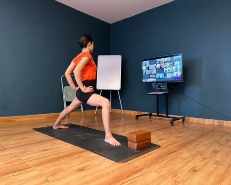 Student practicing an online yoga class at home with live instructor on screen